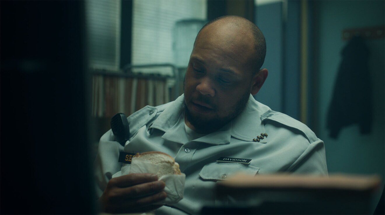 An screenshot image of a security guard in the security office during the Amazon Prime commercial where he becomes a chef. 