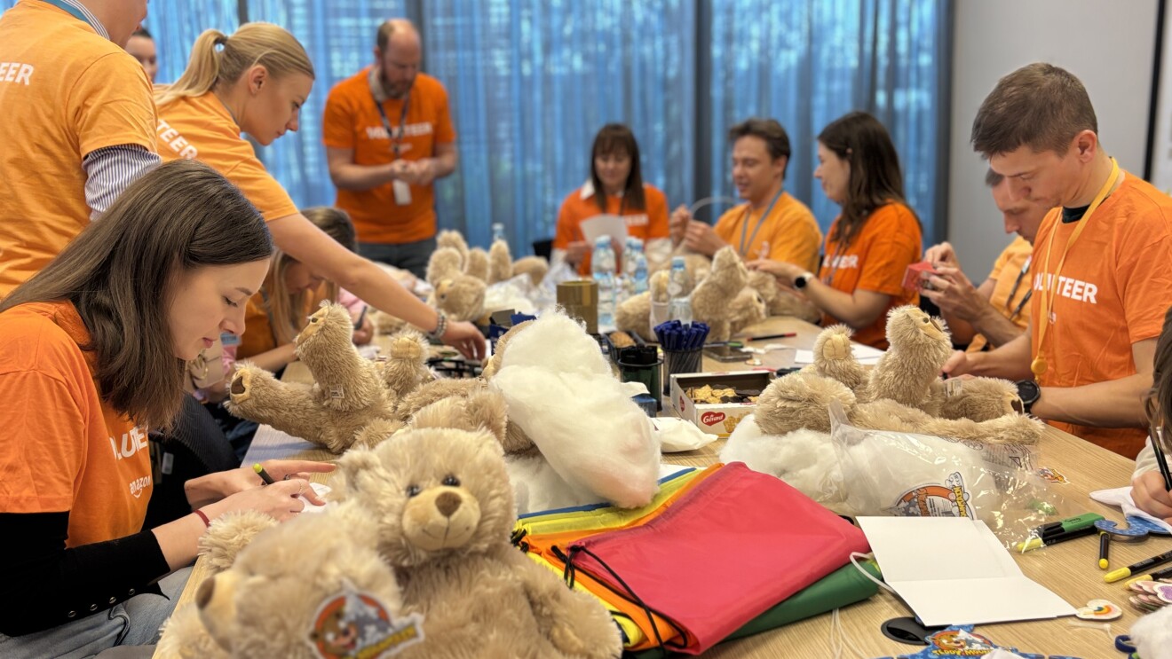 Volunteers in orange shirts assembling teddy bears at a table in Poland