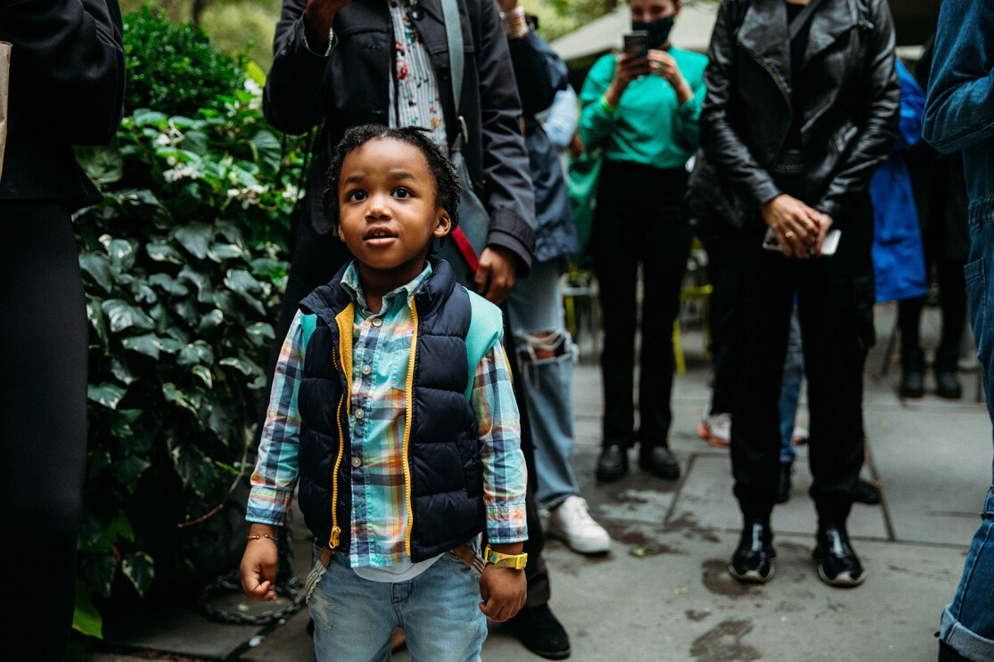 An image of a boy standing in a park and smiling softly while looking around him.