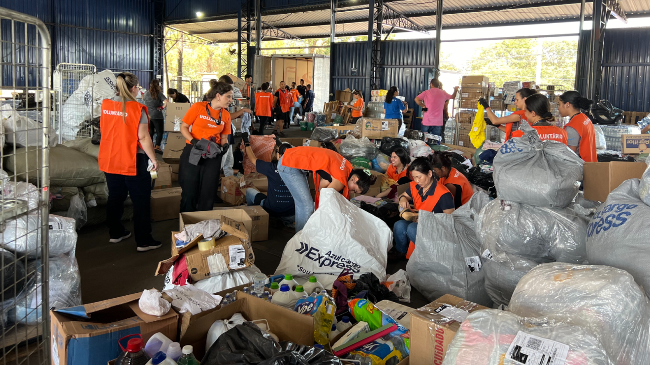 Amazon volunteers wear orange "Amazon volunteer" vests and go through hundreds of bags of donations in a warehouse.