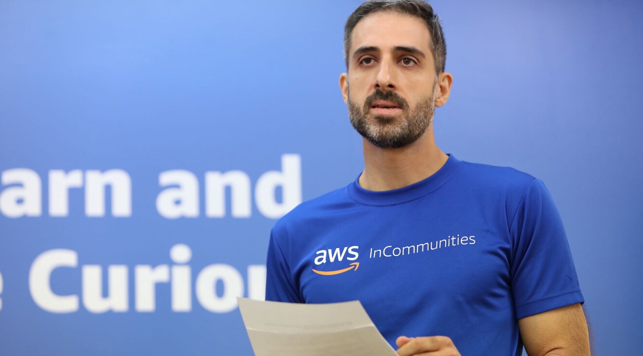 AWSのロゴが入った青いTシャツを着ている顎髭のある男性