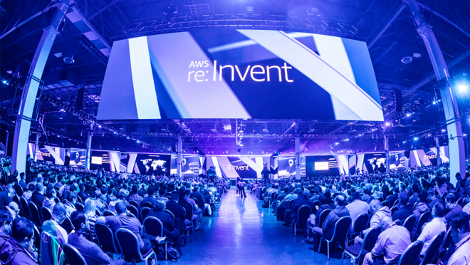 AWS re:发明会议,视图显示数百个人坐在椅子上的会议。一个巨大的屏幕悬挂在他们上方,整个空间充满了蓝光。