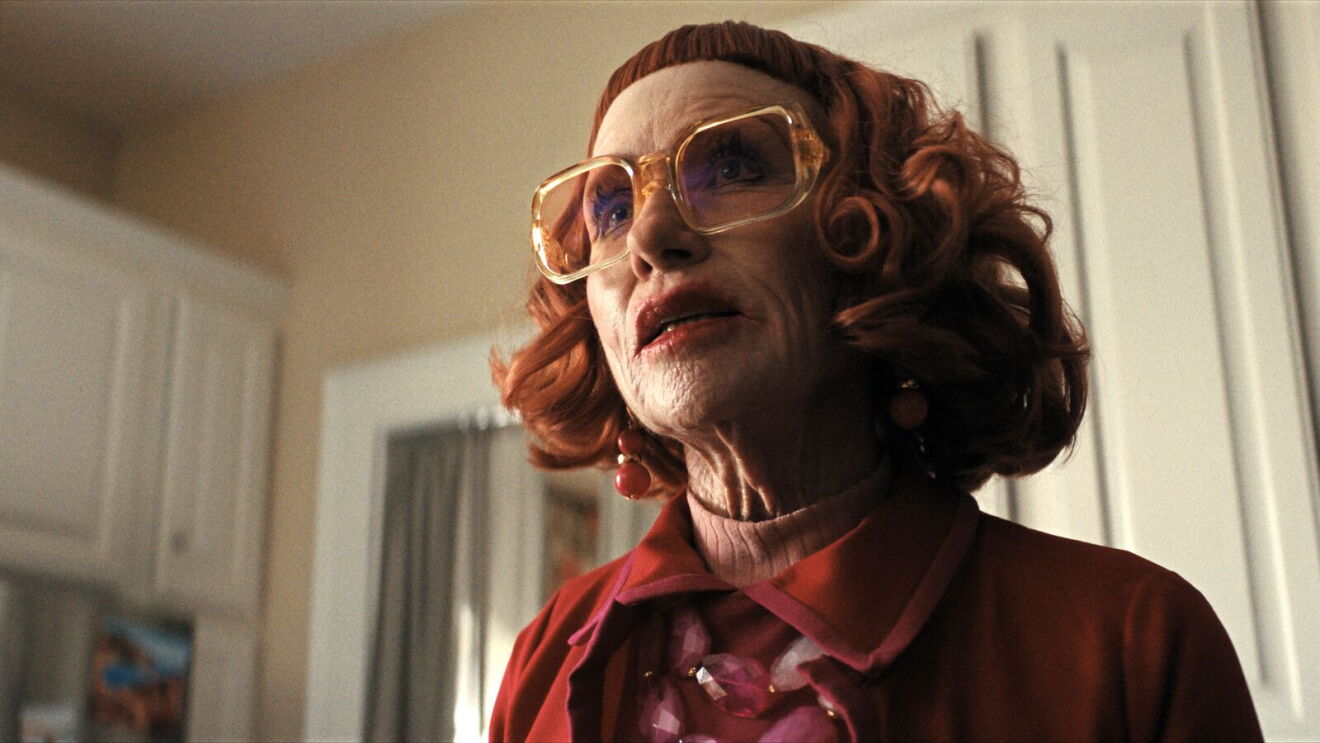 A woman with bright red hair wears glasses