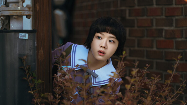 Yeo Eui-ju dressed in purple school uniform hiding behind the bush