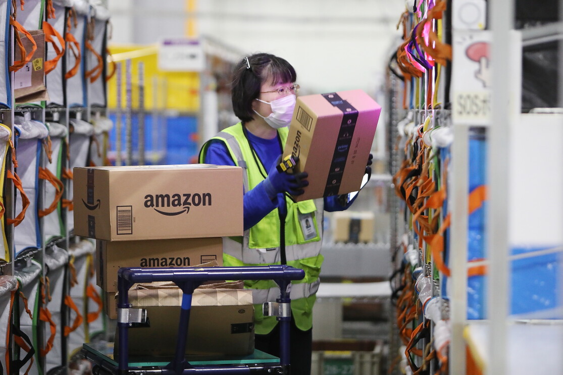 仕分け棚に商品の段ボールを入れようとしている女性。入れる棚の部分が光っている