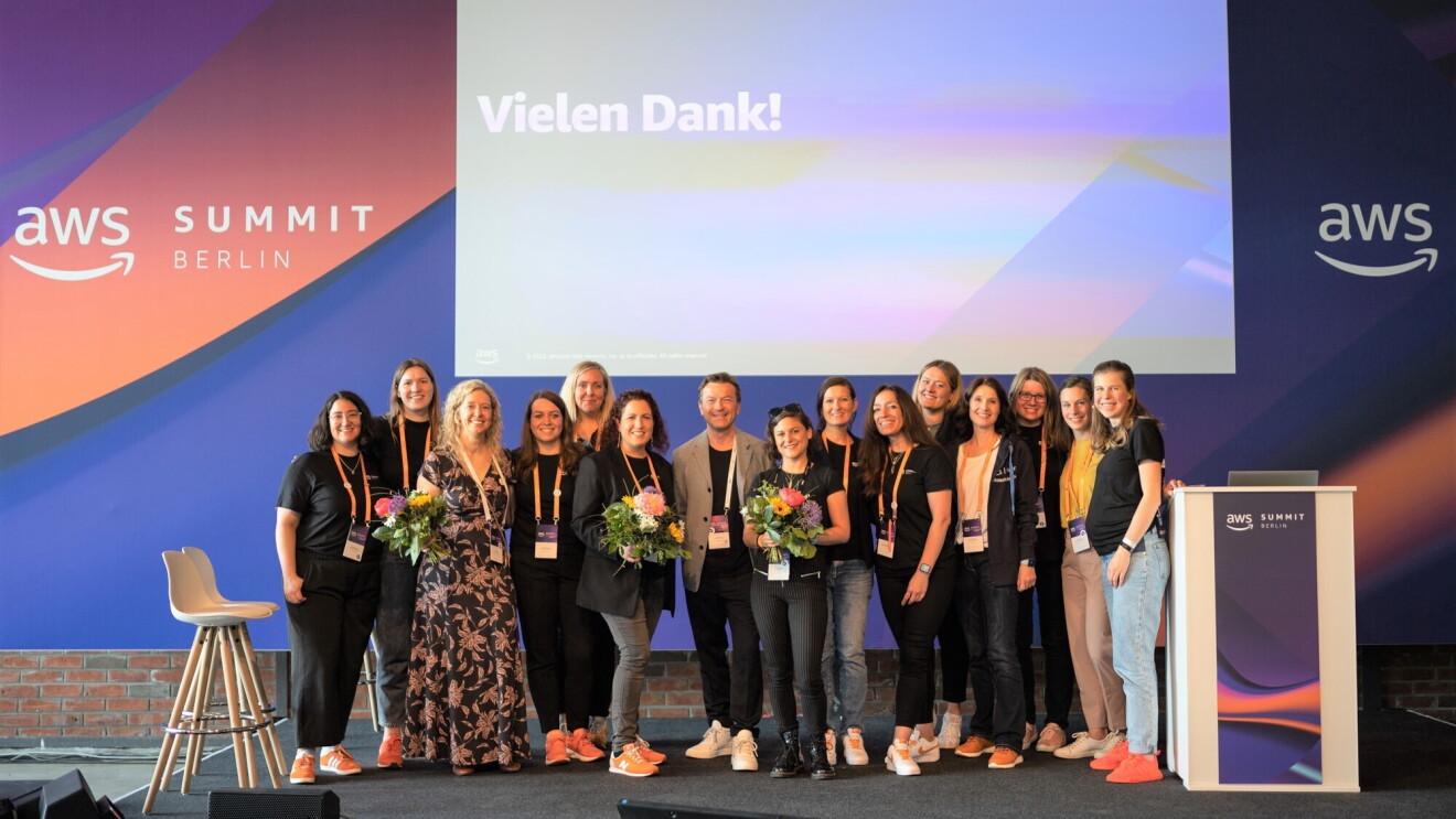 Gruppenbild von Klaus Bürg, Managing Director DACH bei AWS und dem GetIT Team aus Deutschland beim bedanken für die Präsentationen der Schulen auf dem AWS Summit in Berlin 2022. Die Gruppe steht auf einer Bühne und im Hintergrund ist "Vielen Dank" sowie "aws SUMMIT BERLIN" zu erkennen. Einige Frauen halten Blumensträuße.