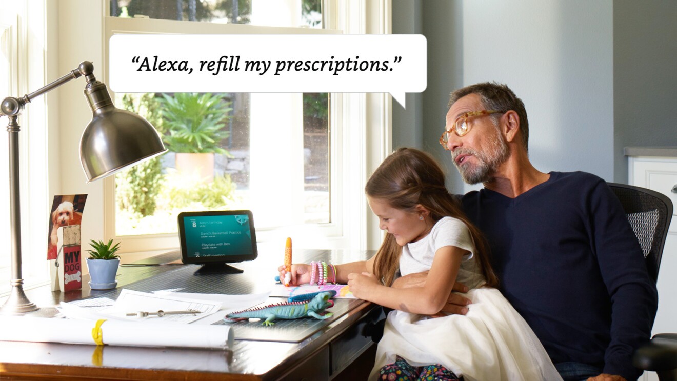 A man sits at a chair at his desk with his granddaughter on his lap. The granddaughter is drawing. A world bubble above the grandfather shows he is asking Alexa to refill his prescriptions. 