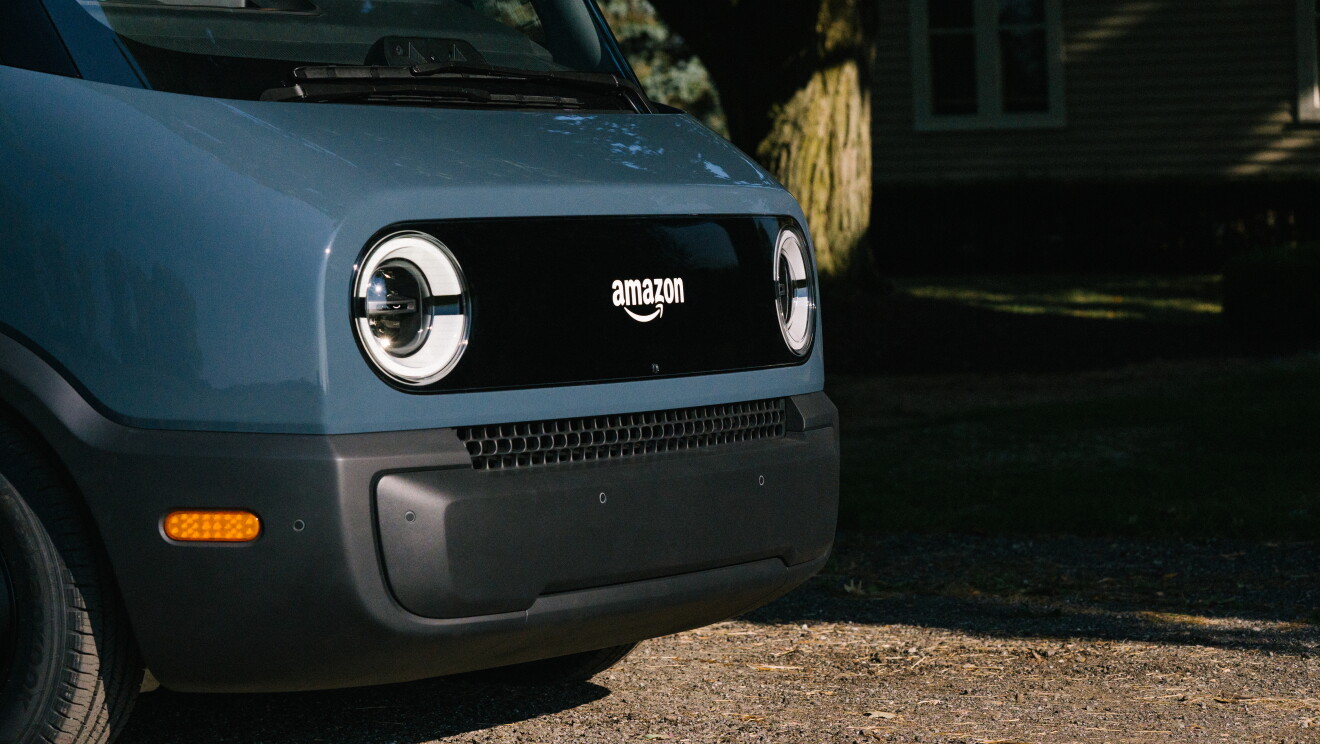 Primer plano de la parte frontal de la furgoneta Rivian. Aparecen los dos faros en blanco y en el centro del logo de Amazon también en blanco. La parte inferior de ventilación es de color negro. 

