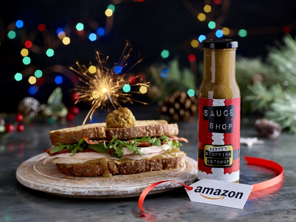 A sandich containing turkey and stuffing balls, next to the stuffing ketchup on a dinner table with an Amazon Label. There is also a sparkler sticking into the sandwich. 