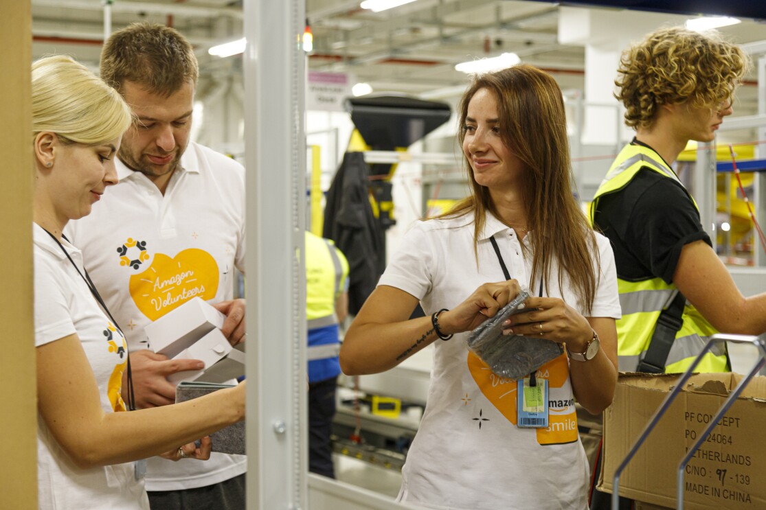 3 Mitarbeiter in T-Shirts mit Aufdruck "Amazon Volunteers" beim Packen.