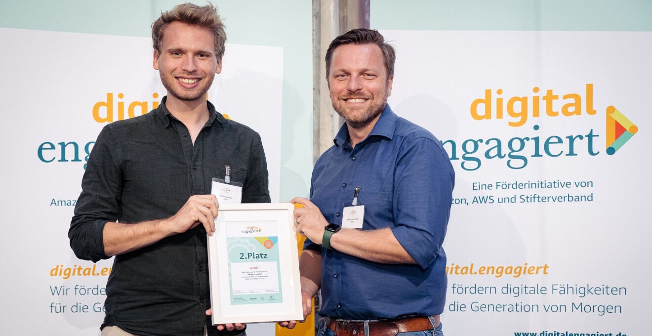 Felix Erdmann und Thomas Bartoschek (v.l.) von re:edu stehen auf der digital.engagiert-Bühne und halten ihre Urkunde für den zweiten Platz in die Kamera.