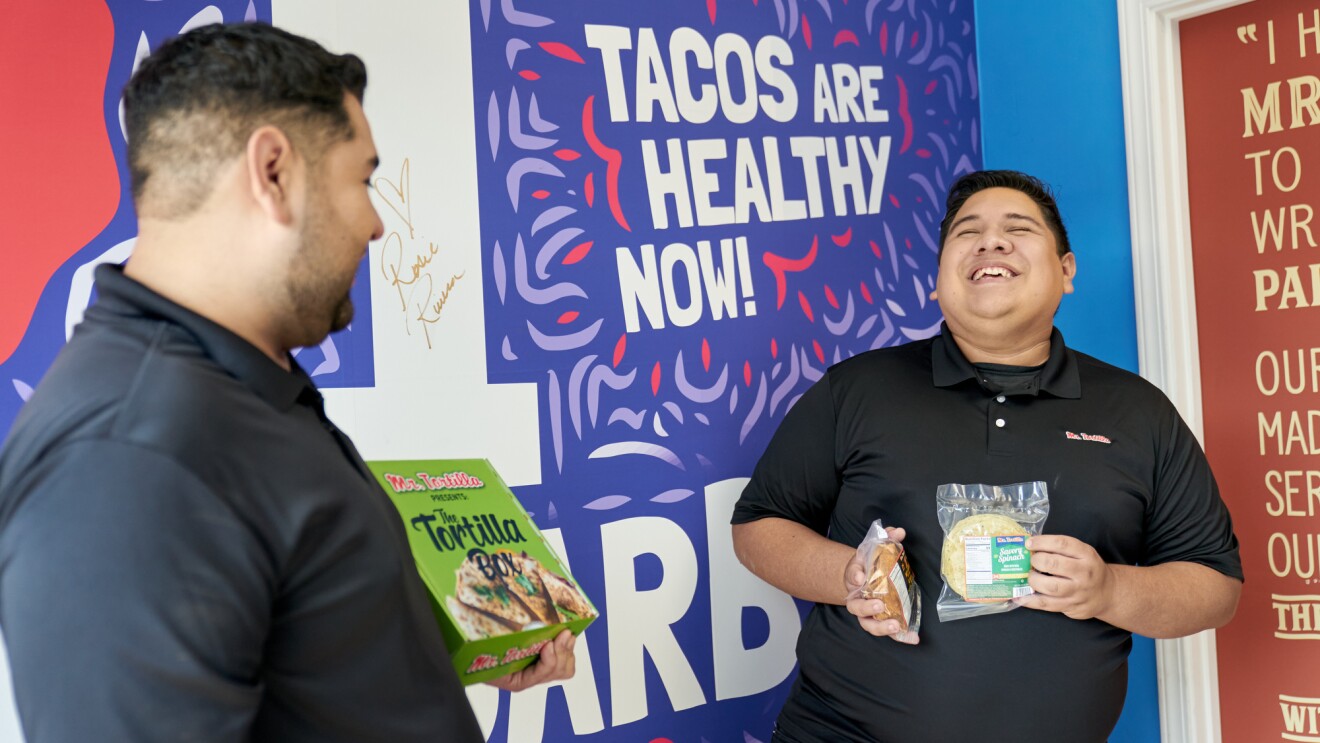 Ronald and Anthony  hold their products in front of a Mr. Tortilla promotional sign.