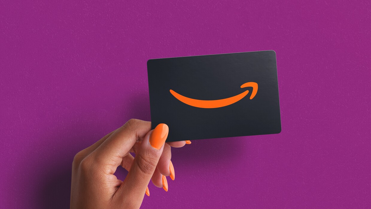 A hand with orange nail polish holding up an Amazon gift card against a purple background
