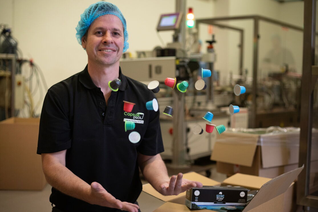 A man throws several coffee capsule packs up in the air in a manufacturing facility