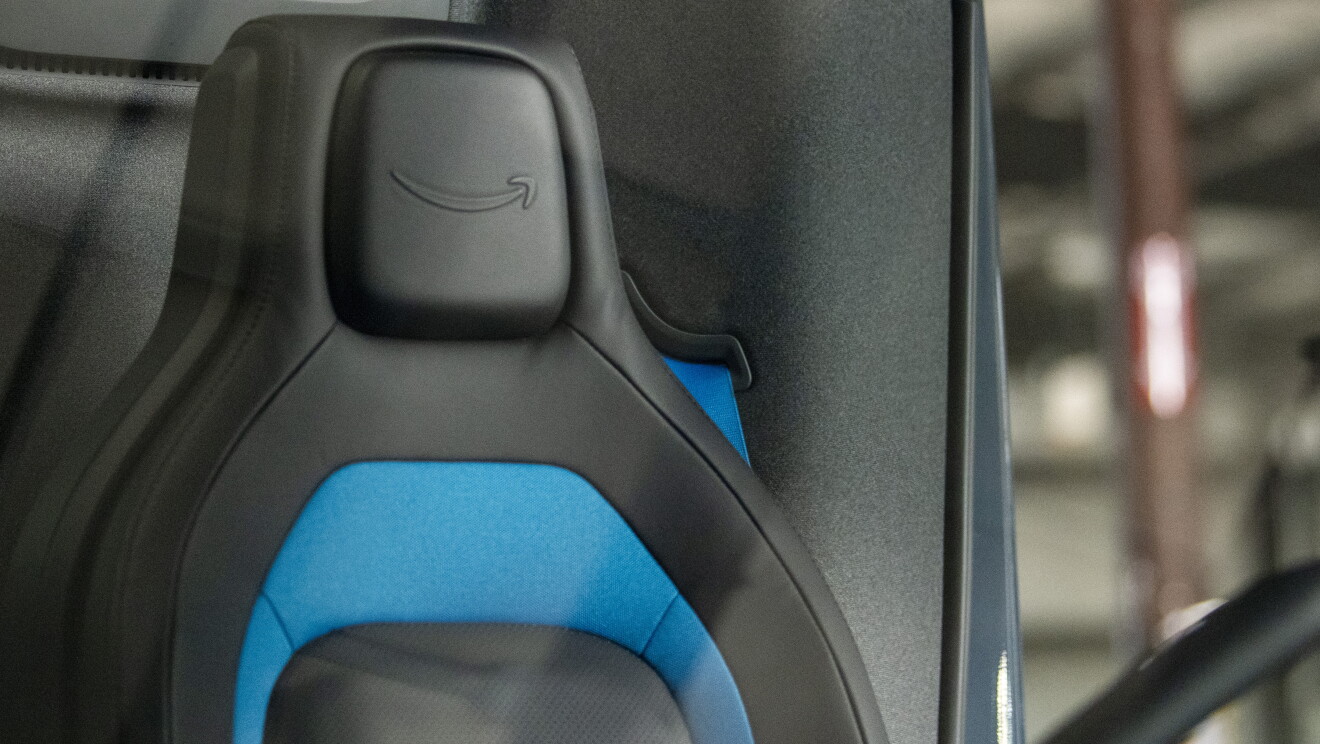 Primer plano del asiento del conductor de la furgoneta Rivian. El asiento es de color negro y azul y a la altura de la cabeza está el logo de Amazon. 