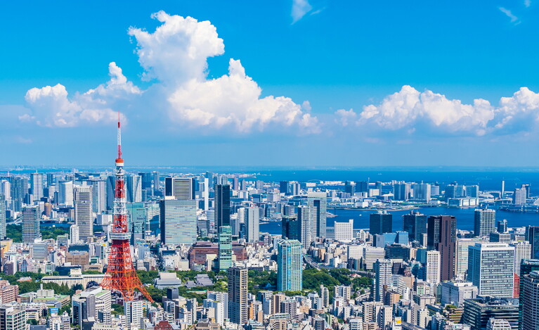 青空の下に広がる東京の街並み。左側に東京タワー、右方向は海。