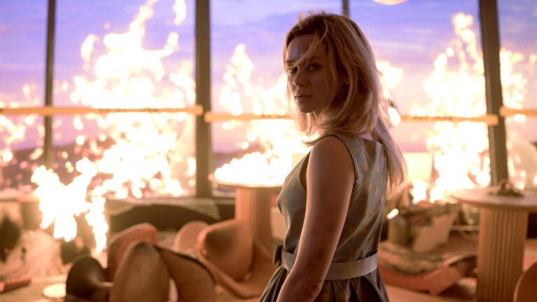 Woman in sleeveless dress standing amid flames engulfing room
