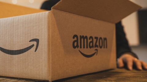 A box with an Amazon smile on it. A woman's hand is visible behind the box. 