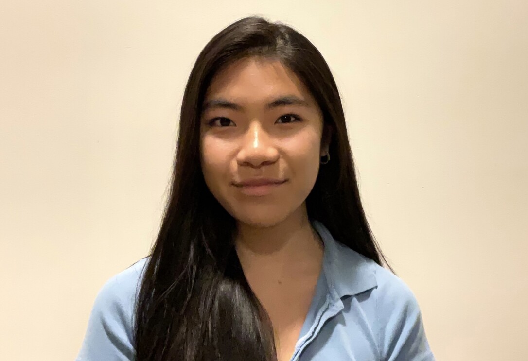 A headshot image of a young woman. There is a white wall in the background behind her.