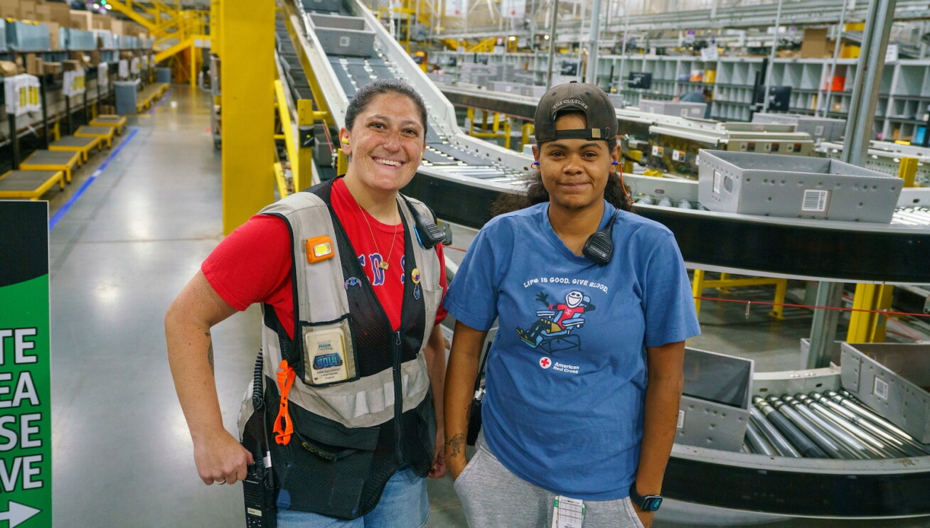 Two Amazon employees smile in front of a conveyor belt at Amazon BDL4.