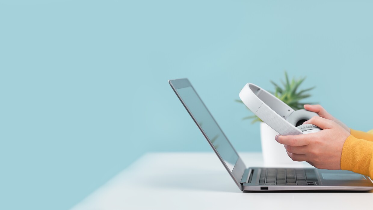 Picture of a laptop with person holding headphones on white desk