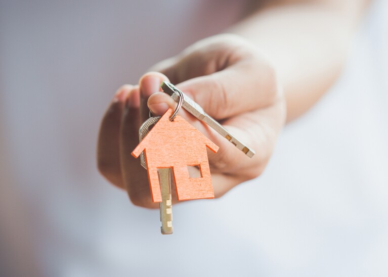 A woman's hand holding a set of keys with a keychain that shows a house on it. 