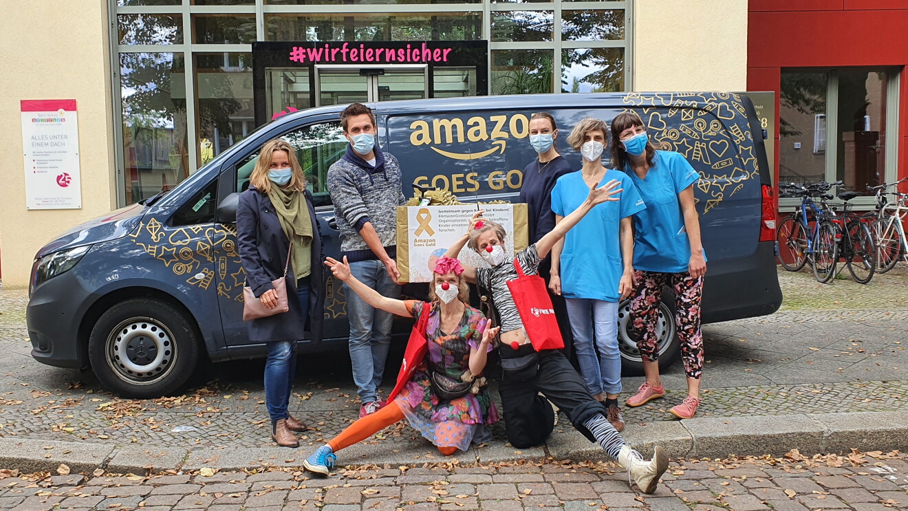 Amazon Mitarbeiter:innen, Rote Nasen Clowns und Krankenhaus Mitarbeiter:innen vor dem mit "Amazon goes gold" beschrifteten Liefervan