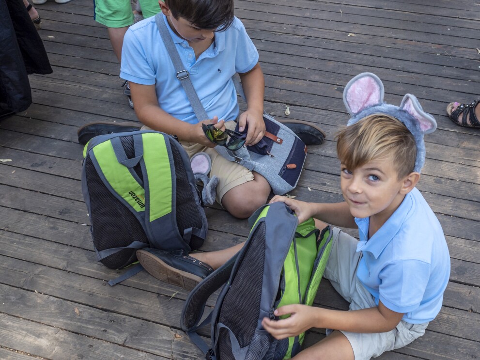 Zwei Kinder sitzen am Boden. Beide tragen einen Haarreif mit Mäuseohren. Vor ihnen der Rucksack von Amazon, den jeder der kleinen Gäste erhalten hat.