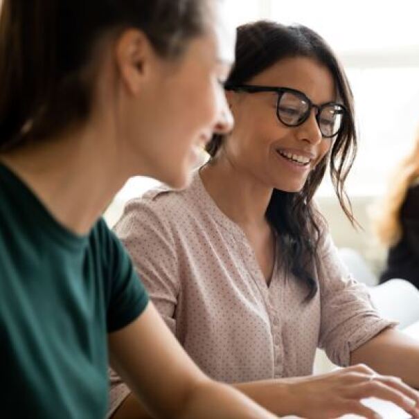 zwei junge Frauen sitzen vor dem Computer und besprechen sich