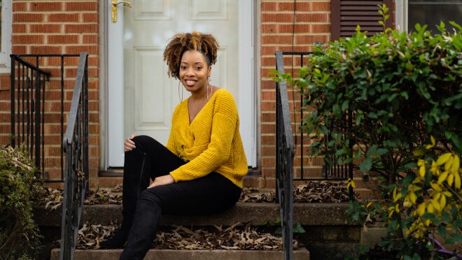 一个女人,水晶Swain-Bates,坐在前面一步的砖家。她水黑靴,黑色裤子,芥末黄色的毛衣,和大好的篮球。