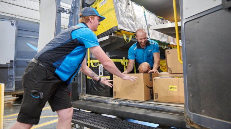 Two Amazon workers smile while loading a delivery van