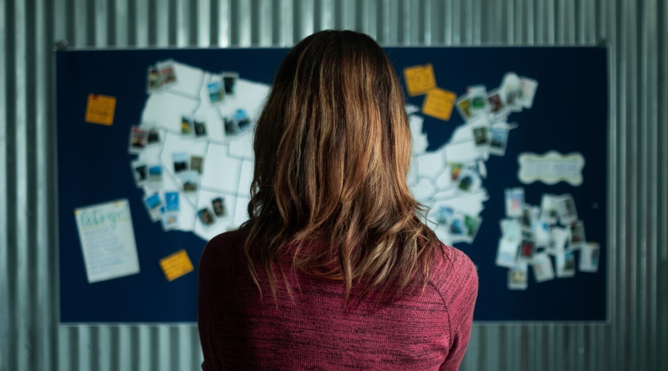 A photo of a person looking at the map of the United States. On that map, images are pinned on certain cities.