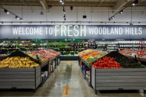 Produce section of a grocery store with the words "WELCOME TO FRESH WOODLAND HILLS" on the back wall.