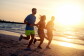 Two men and a woman run on a beach at sundown.
