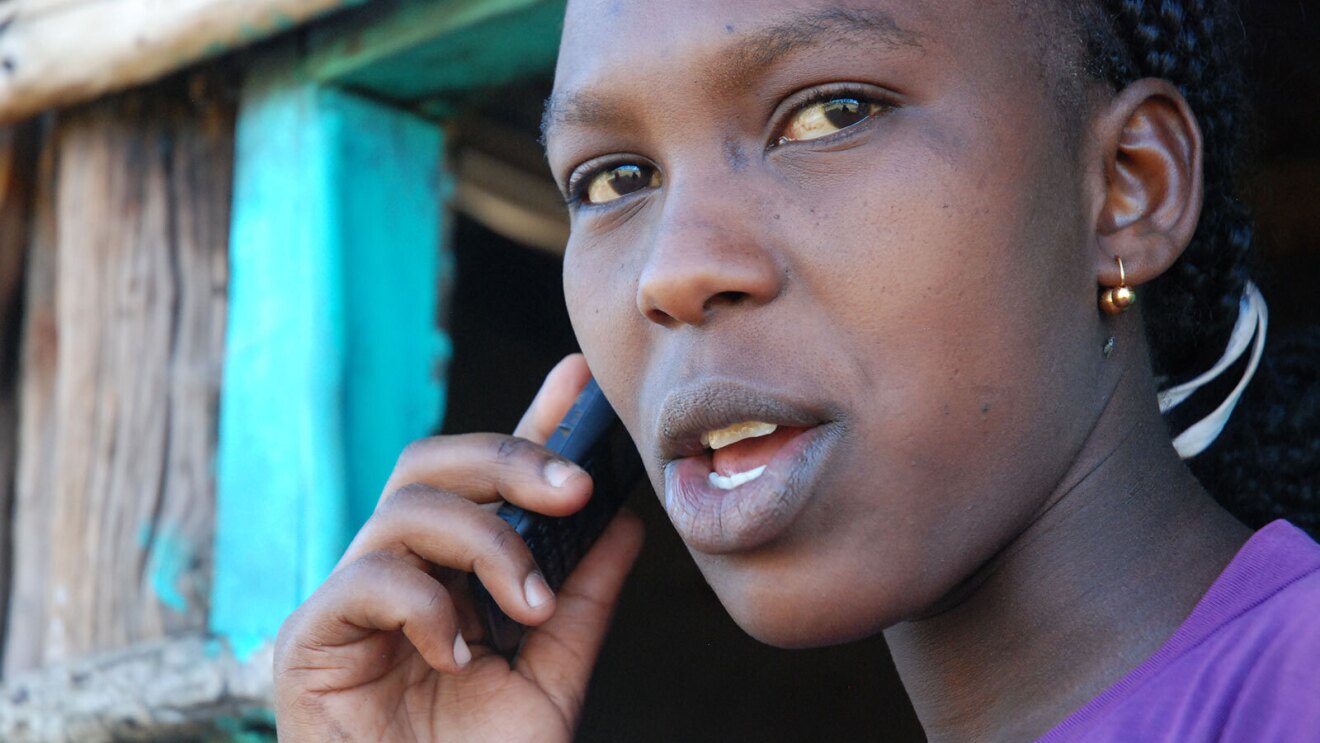 A close up image of a woman holding a phone up to her ear while speaking.