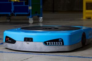 An image of Amazon's new Titan robot. It's blue, plate-like robot with black details, including a camera on the front, a name plate that says "T333333" and a large, circular plate on top. 