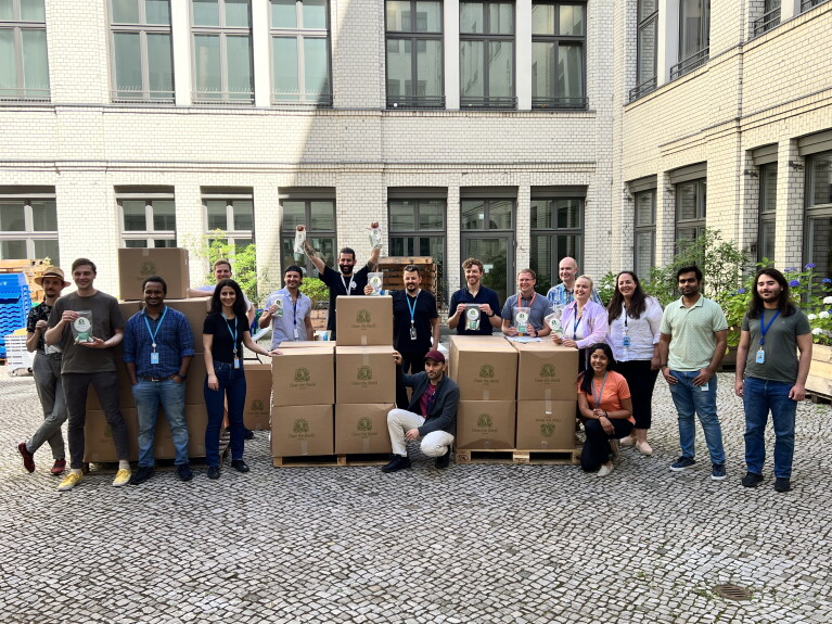 Gruppenfoto von Berliner Mitarbeiter:innen in einem Innenhof mit Kisten, die Hygiene-Kits für Menschen enthalten, die vom Krieg in der Ukraine betroffen sind.