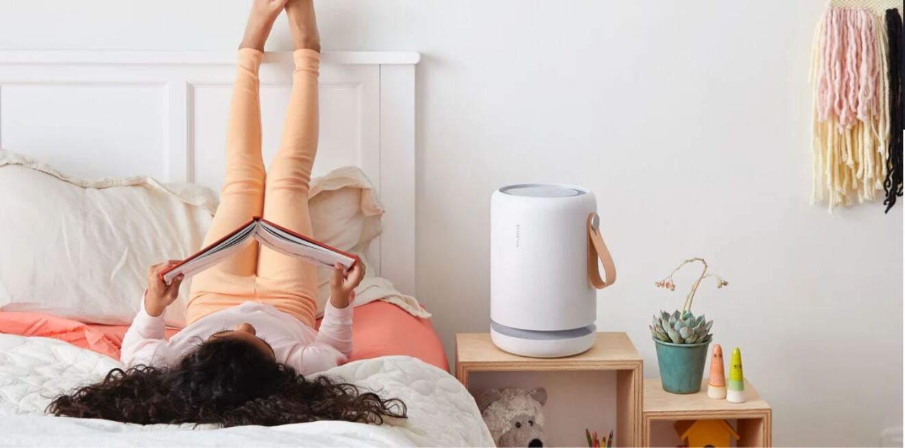 Ein Mädchen liegt auf einem Bett und ließt. Neben ihr steht eine große weiße Alexa.