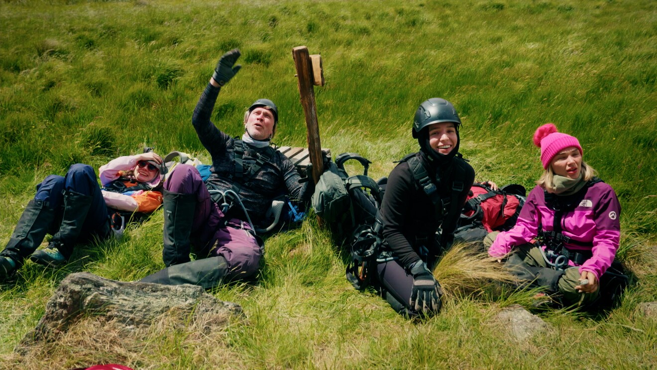 Vier Wanderer ruhen sich auf einer Wiese aus, einer zeigt nach oben.