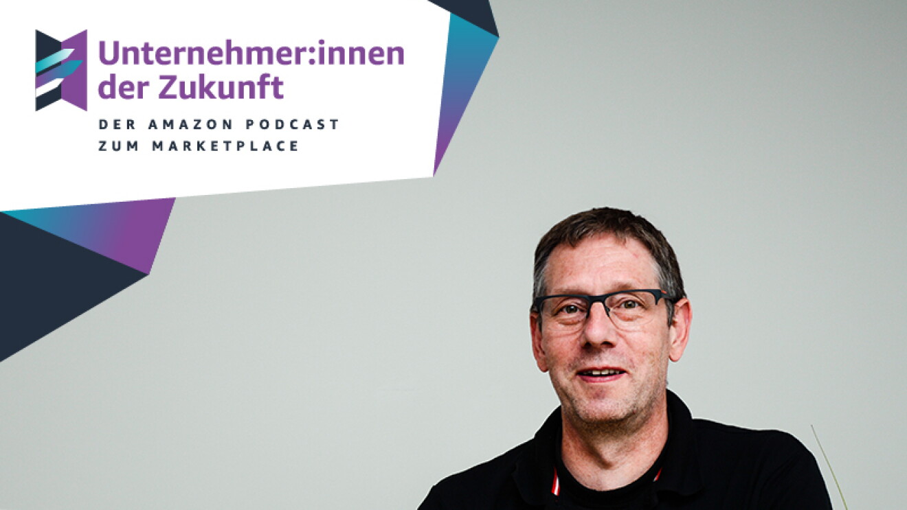 Ein Mann mit schwarzen Haaren und einem schwarzen T-shirt sitzt an einem Tisch. Vor ihm steht ein schwarzer Laptop.