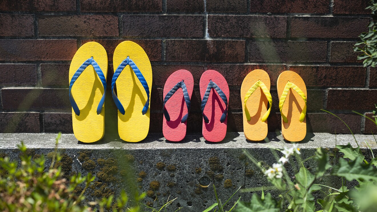 レンガの塀の前に並べられたカラフルなビーチサンダル。大人用と子ども用
