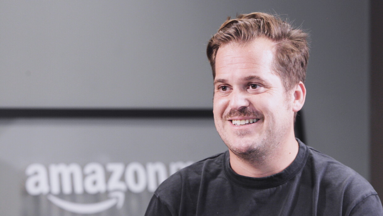 Primo piano di Giovanni Malacarne. Indossa una t-shirt nera, sullo sfondo si intravede il logo di Amazon Music 