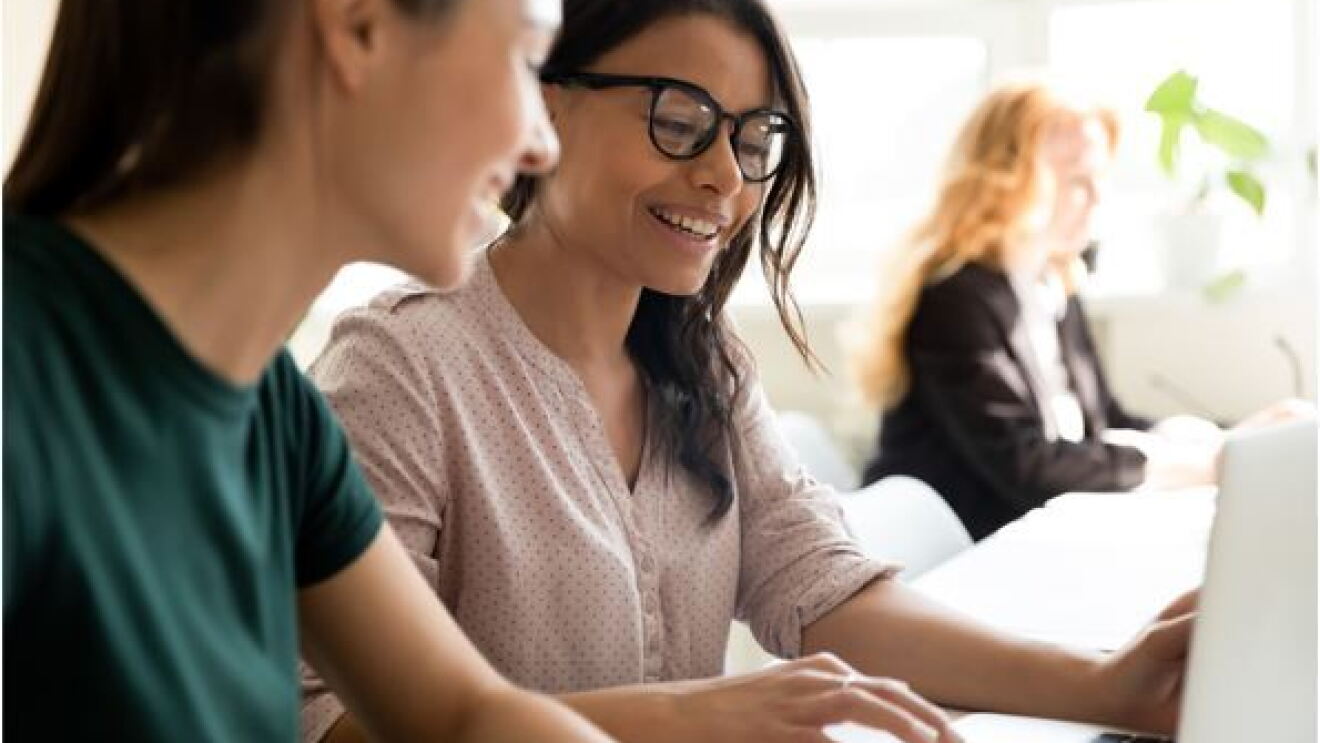 zwei junge Frauen sitzen vor dem Computer und besprechen sich