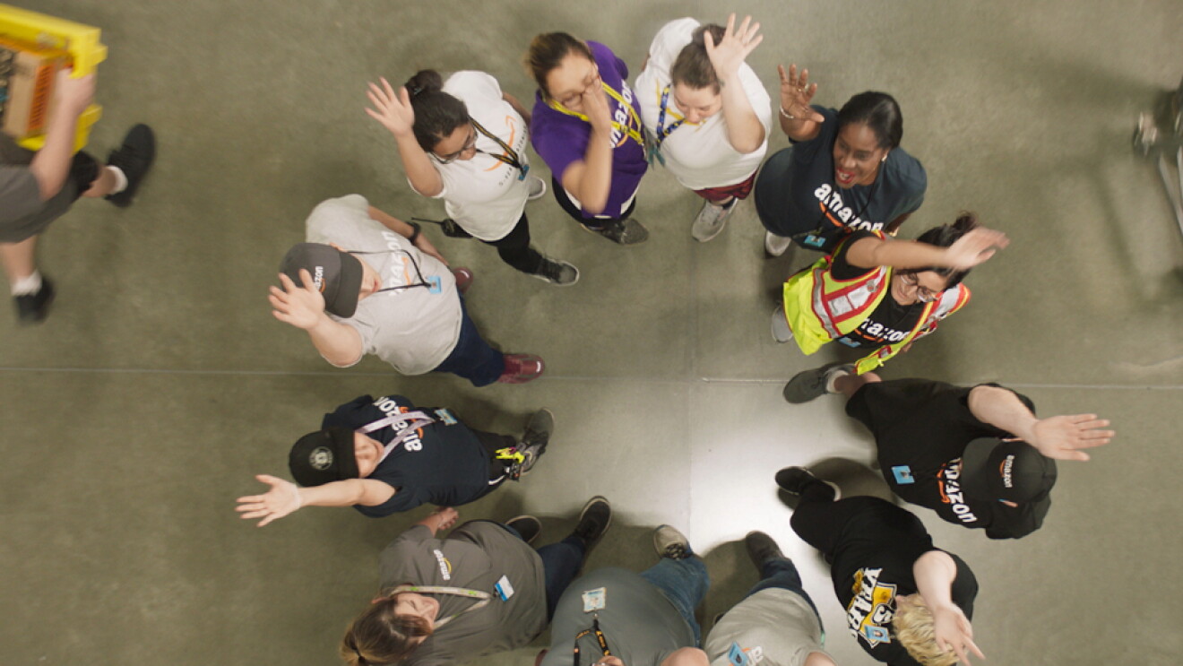Overhead shot of people standing in a circle. They each have one hand raised.