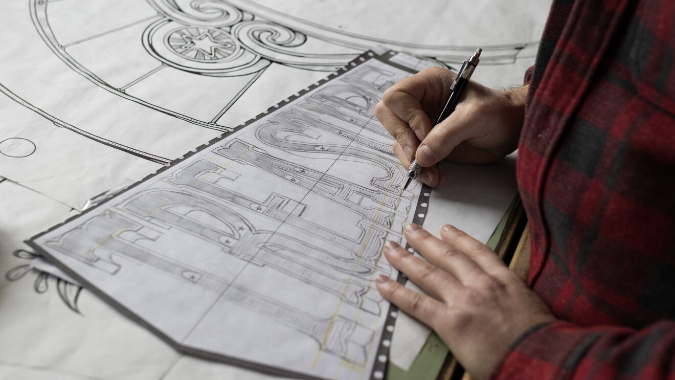 Kyler Martz in his Seattle studio. He is drawing the word TREASURE onto a large piece of paper.