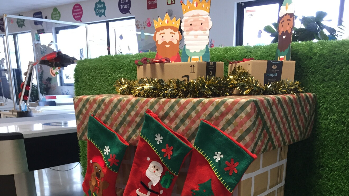Adorno navideño de DQA4.  Chimenea hecha de cartçon con fuego simulados y los ters reyes magos encima. Del árbol cuelan tres calcetines de color rojo. 