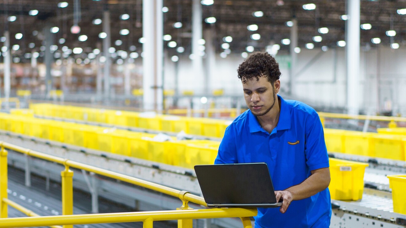 一个穿着蓝色球衣在笔记本电脑上工作在一个大的挑高空间。黄色塑料手提袋身后,一直延伸到远方。