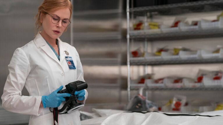 Scientist in lab coat examining handheld device near shelves of samples