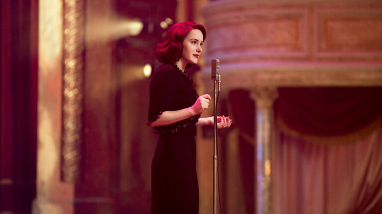An image of Mrs. Maisel from the Amazon series "The Marvelous Mrs. Maisel" talking through a microphone.