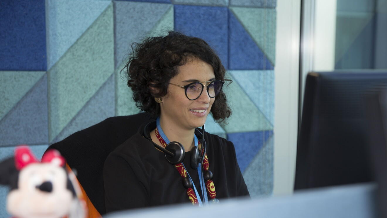 Sarah Beddini, Head of Vendor Management della sezione Giochi & Giocattoli di Amazon, siede alla sua scrivania, di fronte allo schermo del PC. In primo piano, fuori fuoco, un peluche del personaggio di Minnie. 